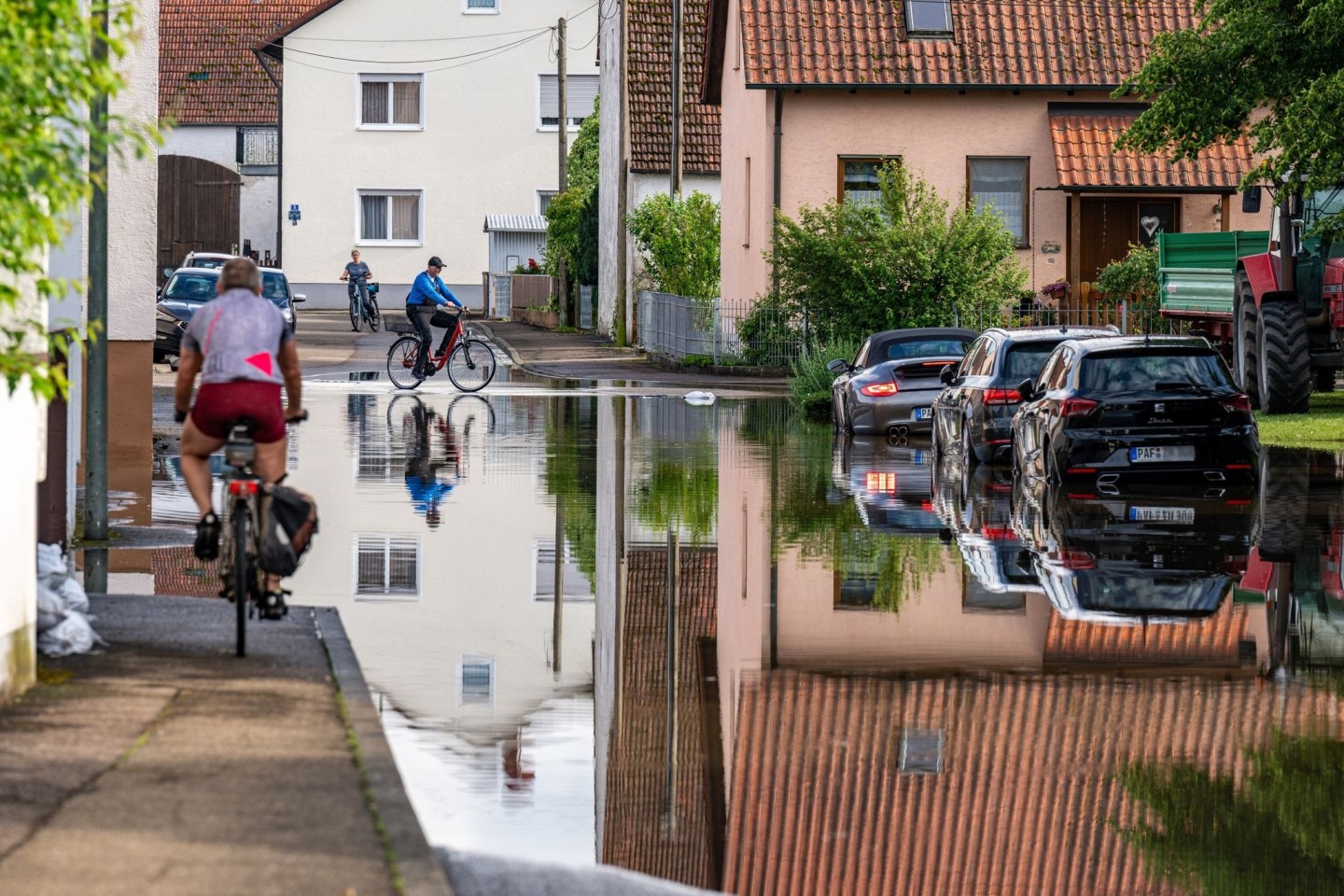 Radler fahren durch eine überflutete Straße. Im Bereich der Gemeinde Baar-Ebenhausen war ein Damm an zwei Stellen geborsten.