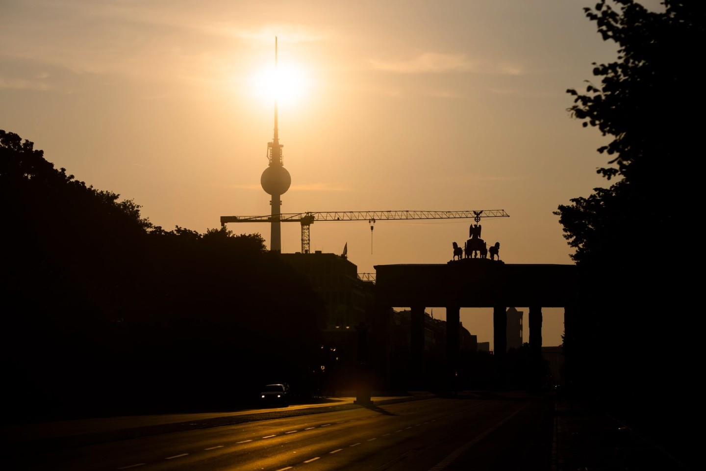 Das Brandenburger Tor und der Fernsehturm sind im Gegenlicht der aufgehenden Sonne zu sehen. Am Montag zeigt sich laut Vorhersage meist die Sonne, höchstens wird es locker bewölkt.